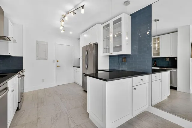 a kitchen with granite countertop a refrigerator a sink and white cabinets