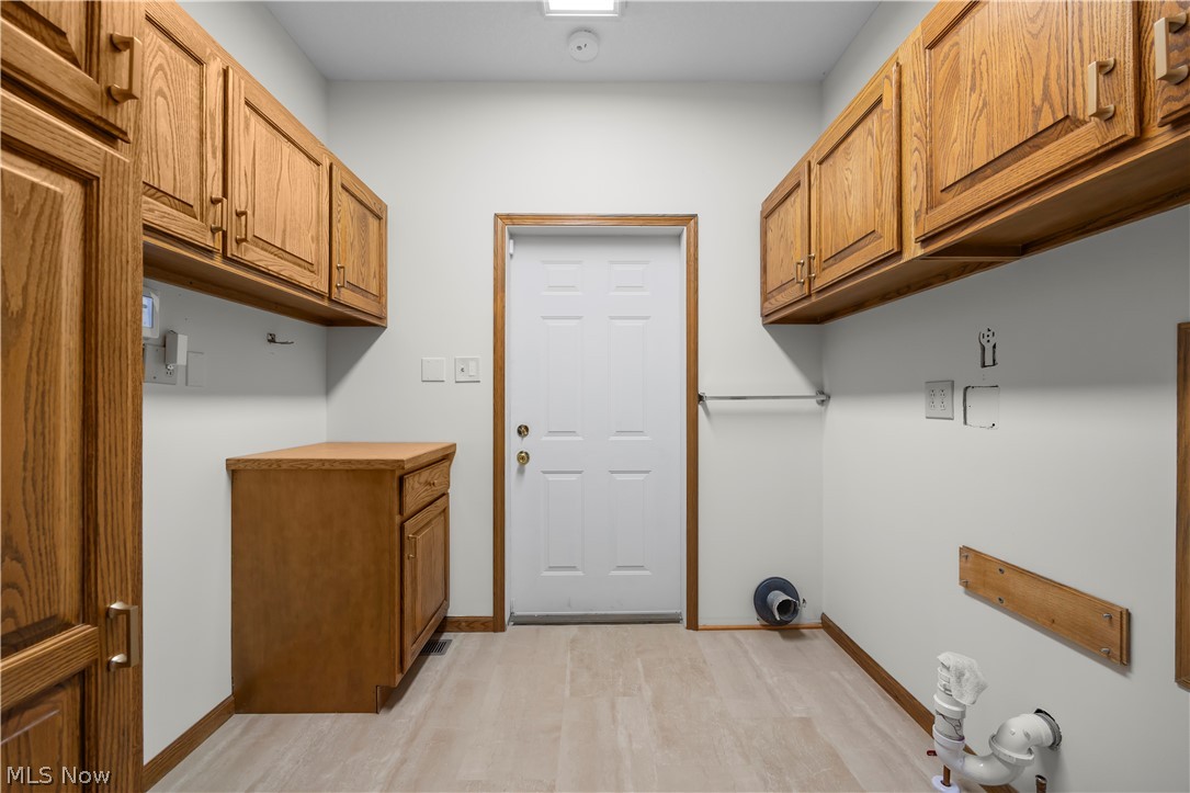 51488 Peck Wadsworth Road Wellington, OH 44090 - Photo 42 of 50 Utility room featuring wood-finish cabinetry, a built-in countertop, a white paneled door, and light-toned flooring