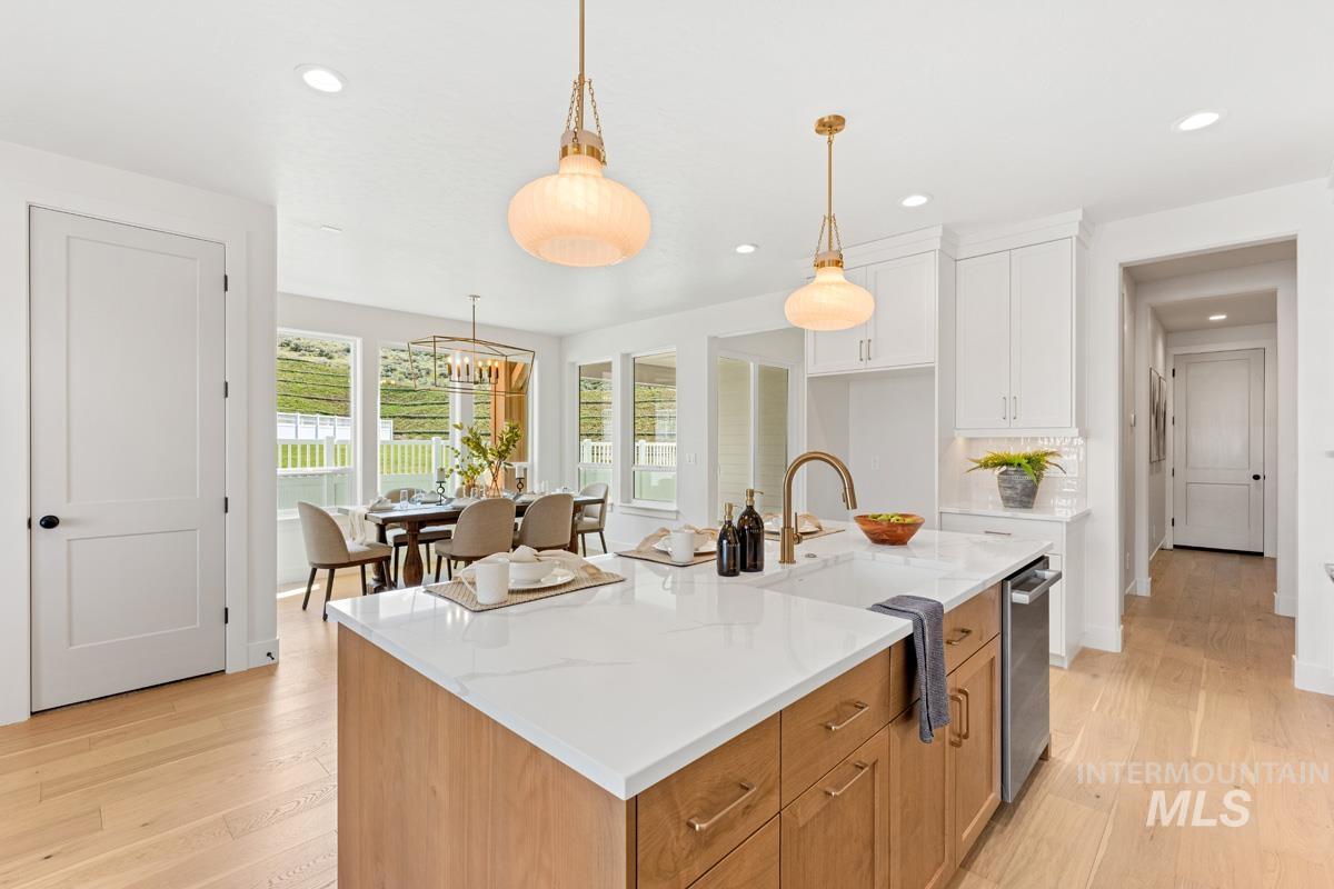13374 North Spring Creek Way Boise, ID 83714 - Photo 8 of 49 Kitchen with two tone cabinetry, light wood-style floors, a center island with sink, light stone counters, and decorative light fixtures