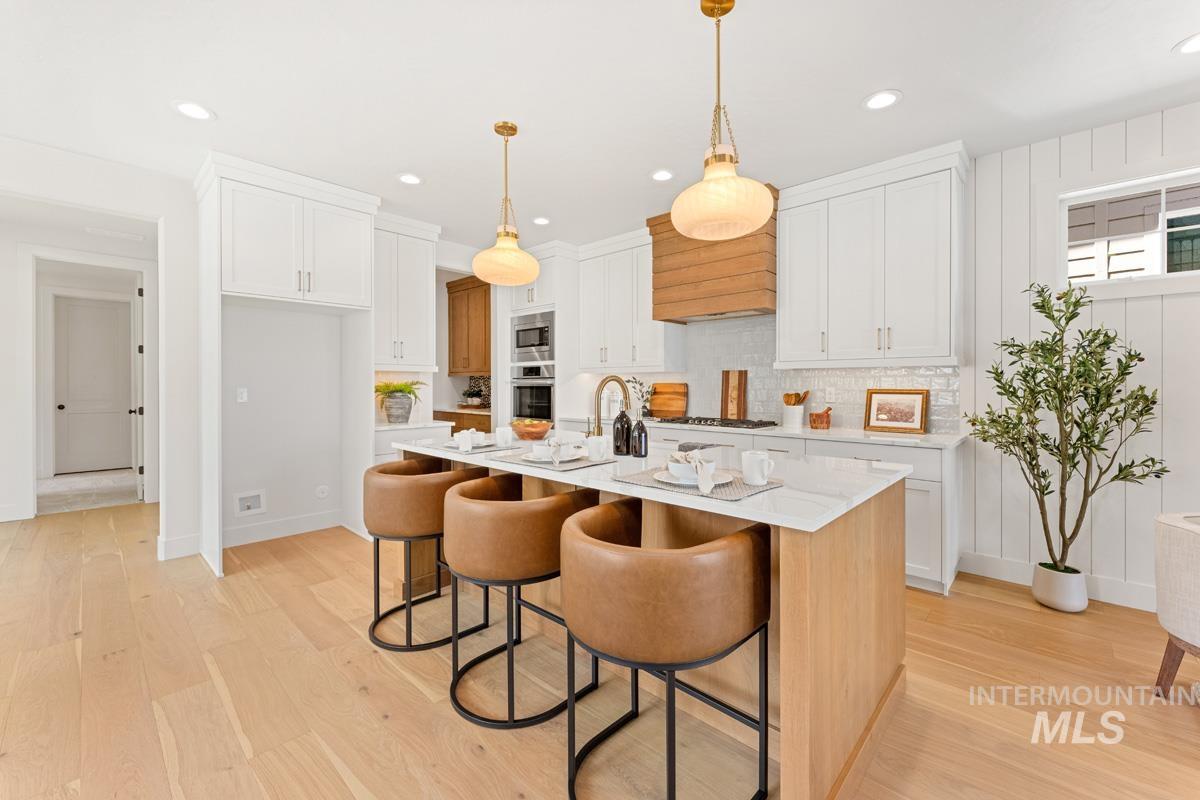 13374 North Spring Creek Way Boise, ID 83714 - Photo 10 of 49 Kitchen with a kitchen breakfast bar, decorative light fixtures, a kitchen island with sink, light wood-type flooring, and two tone color scheme