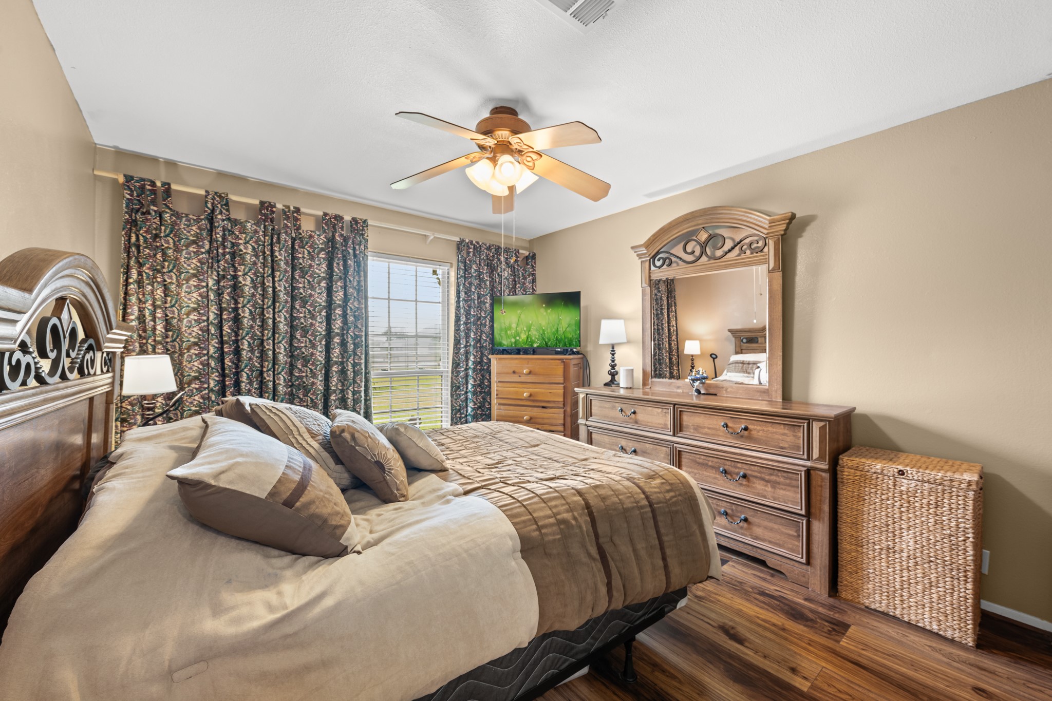 15602 Fir Road Santa Fe, TX 77517 - Photo 21 of 42 Comfortable bedroom featuring warm wood-look flooring, neutral tones, and large windows that fill the space with natural light. Generous room size and ceiling fan create a relaxing retreat with plenty of everyday comfort.