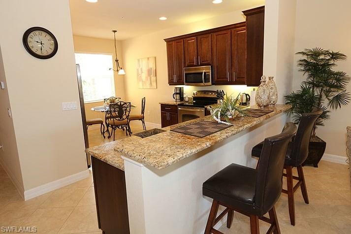 6525 Monterey Point, Unit 203 Naples, FL 34105 - Photo 9 of 25 Kitchen with a kitchen bar, appliances with stainless steel finishes, light stone counters, hanging light fixtures, and light tile patterned floors