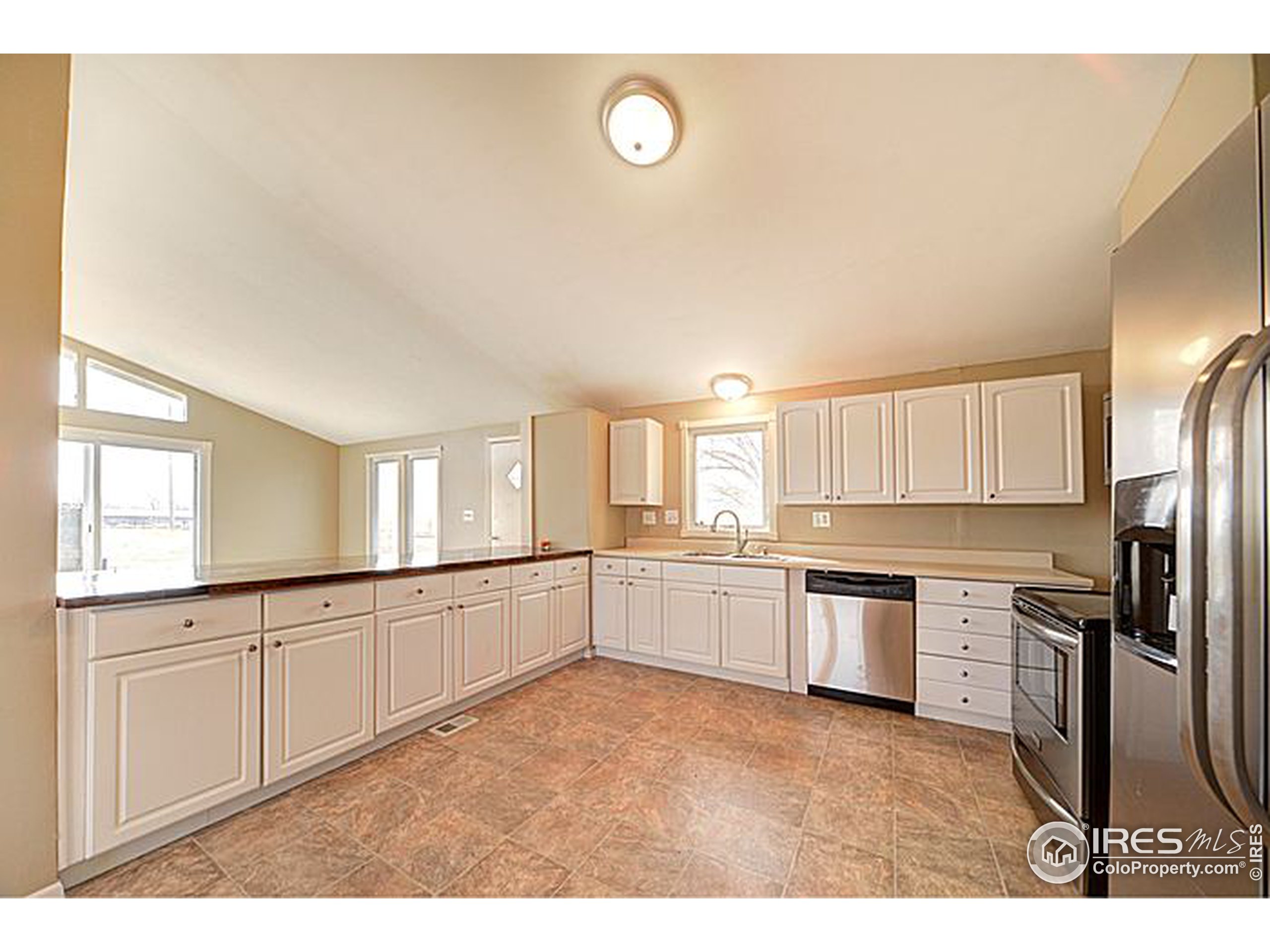 8966 County Road Hudson, CO 80642 - Photo 6 of 25 a large kitchen with a refrigerator a sink dishwasher and white cabinets with wooden floor