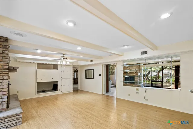 a view of an empty room with kitchen and window