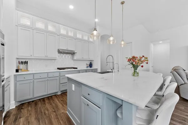 a kitchen with a white center island a sink dishwasher and white cabinets with wooden floor