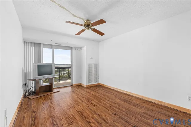 a view of a livingroom with wooden floor a ceiling fan and windows