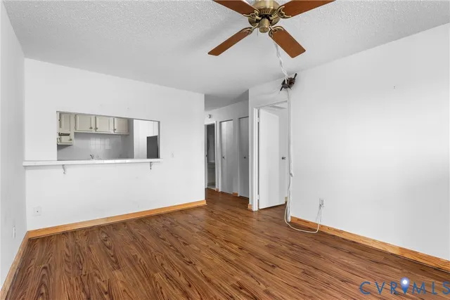 a view of an empty room with wooden floor and a ceiling fan