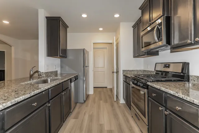 a kitchen with stainless steel appliances granite countertop a refrigerator a stove a sink and a microwave