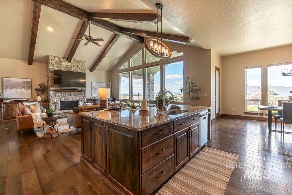 15350 Syrah Court Caldwell, ID 83607 - Photo 11 of 50 Spacious open-concept living area featuring wood-finish flooring, a vaulted ceiling with exposed wood beams, and a floor-to-ceiling stone fireplace