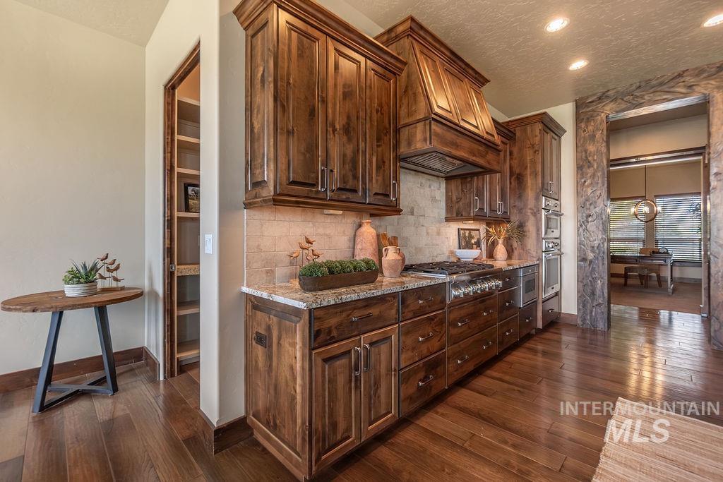15350 Syrah Court Caldwell, ID 83607 - Photo 16 of 50 Gourmet kitchen featuring custom wood cabinetry, granite countertops, tile backsplash, built-in stainless steel double ovens, and a gas range with an ornate wood-paneled vent hood