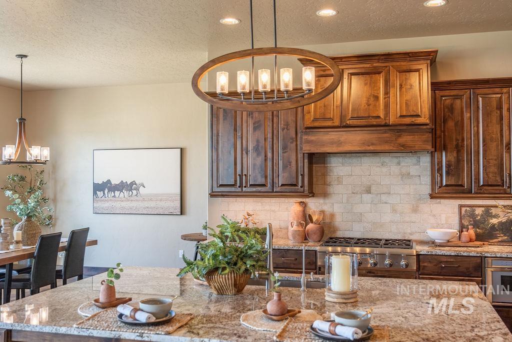 15350 Syrah Court Caldwell, ID 83607 - Photo 18 of 50 Gourmet kitchen featuring a large island with a surface-mounted sink, built-in stainless steel appliances, a tile backsplash, rich wood cabinetry, and an oval chandelier