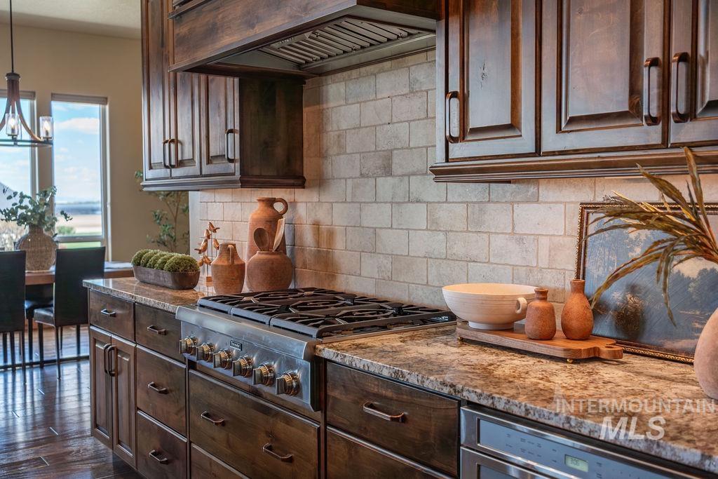 15350 Syrah Court Caldwell, ID 83607 - Photo 20 of 50 Gourmet kitchen featuring dark wood cabinetry, granite countertops, a tiled backsplash, and a stainless steel gas range with a matching range hood