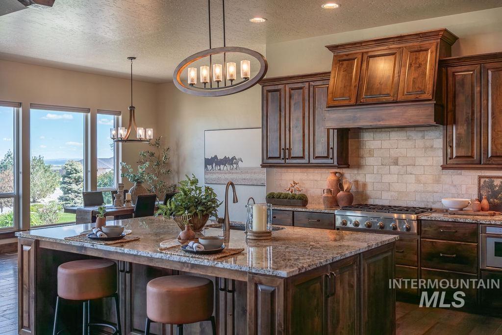 15350 Syrah Court Caldwell, ID 83607 - Photo 21 of 50 Spacious kitchen featuring a large central island with seating, dark wood cabinetry, stainless steel appliances, a tiled backsplash, and recessed and pendant lighting
