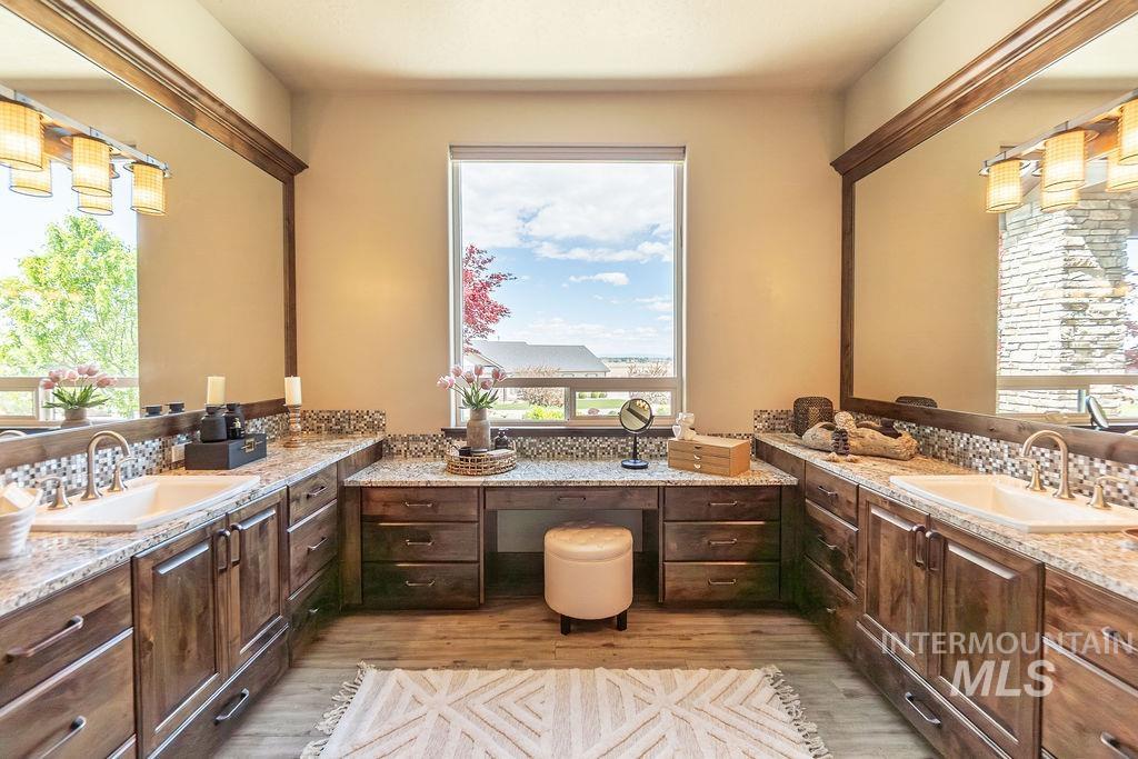 15350 Syrah Court Caldwell, ID 83607 - Photo 33 of 50 Spacious vanity featuring dual sinks, extensive wood cabinetry, granite countertops, mosaic tile backsplash, and a dedicated makeup area beneath a large window