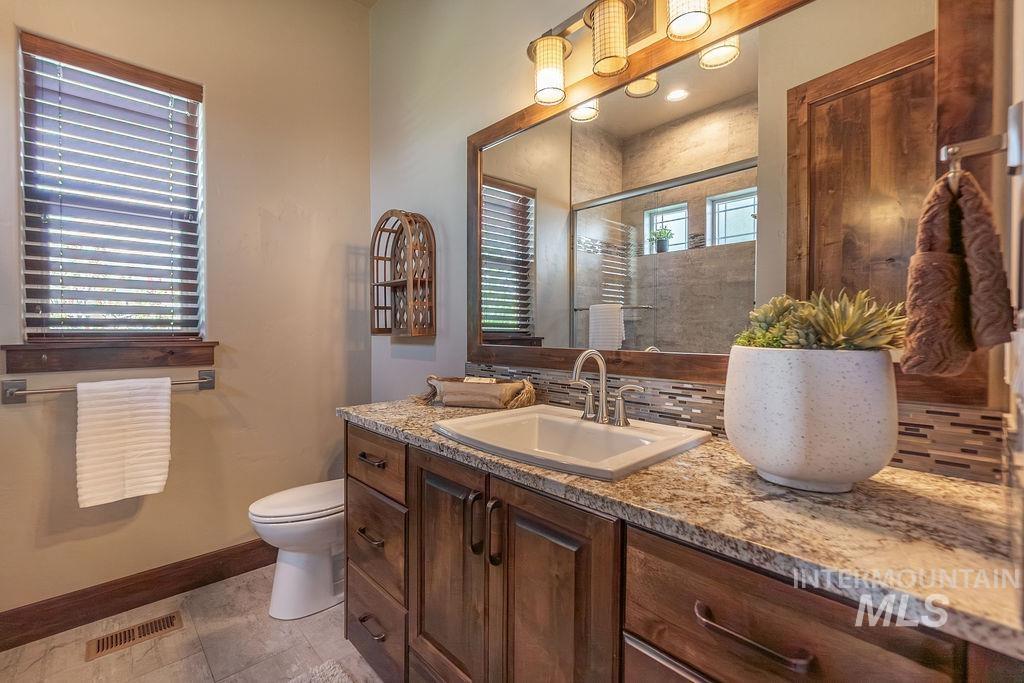 15350 Syrah Court Caldwell, ID 83607 - Photo 43 of 50 Bathroom featuring a wood-finish vanity with an undermount sink, a granite-style countertop, a rectangular mirror with integrated lighting, and a window with blinds