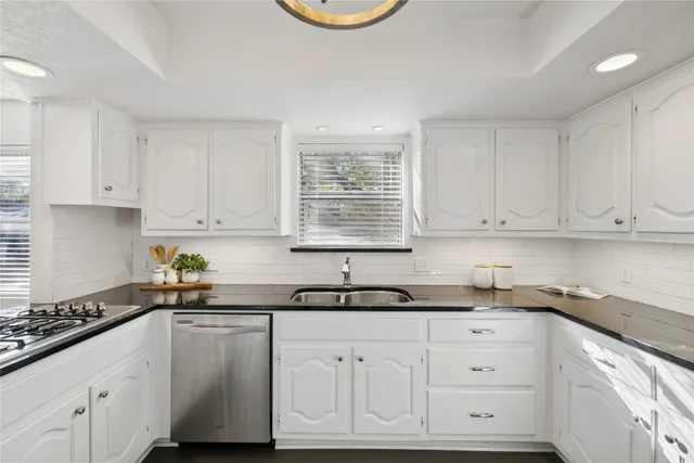 a kitchen with white cabinets appliances a sink and a window