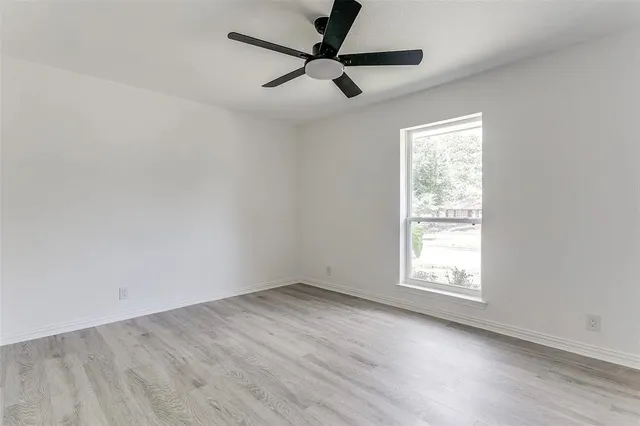 an empty room with wooden floor fan and windows