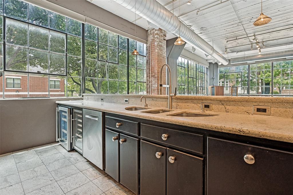 2220 Canton Street, Unit 101 Dallas, TX 75201 - Photo 4 of 20 Industrial-inspired kitchen area featuring a large window wall, exposed ductwork, a dry bar with built-in beverage refrigerators, stone countertops, and black cabinetry