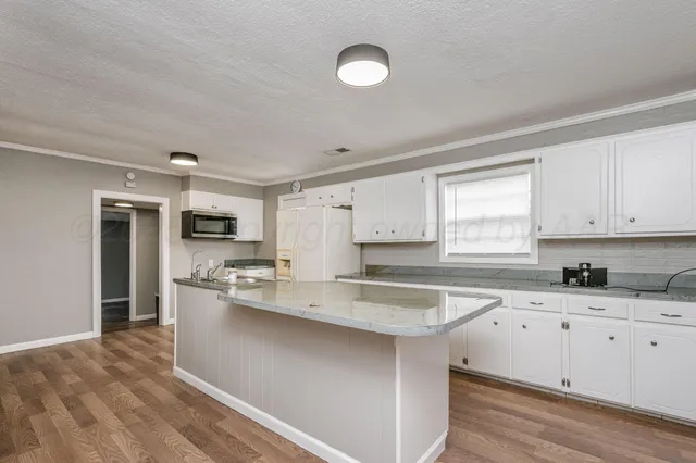 a kitchen with stainless steel appliances granite countertop a sink dishwasher a refrigerator and white cabinets with wooden floor