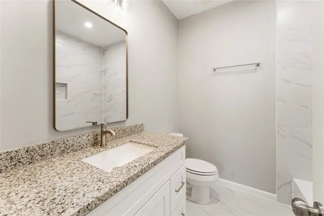 a bathroom with a granite countertop sink a toilet and a mirror
