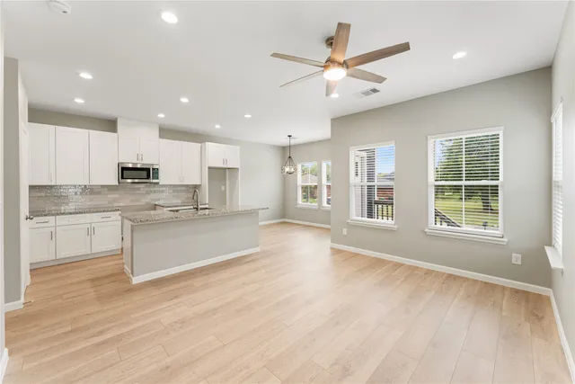 a large kitchen with stainless steel appliances granite countertop a stove a sink and white cabinets with wooden floor