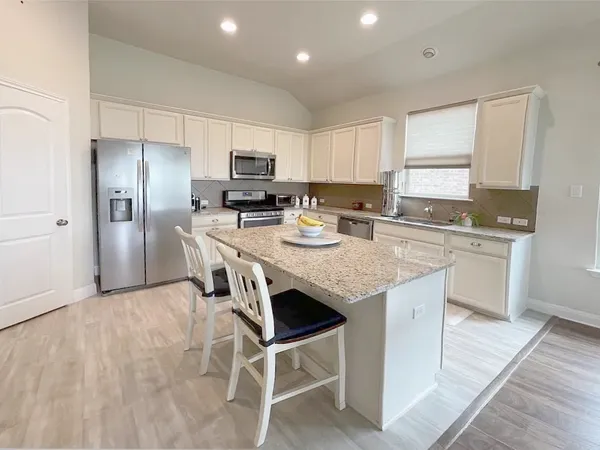 a kitchen with stainless steel appliances granite countertop a stove top oven a refrigerator a sink and a dining table with wooden floor