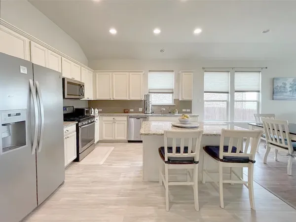a kitchen with stainless steel appliances granite countertop a stove a sink a refrigerator a dining table and chairs