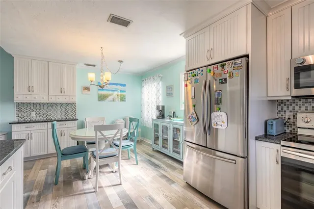 a kitchen with stainless steel appliances a refrigerator a stove a dining table and chairs with wooden floor