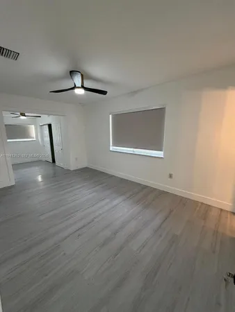 a view of an empty room with wooden floor and a ceiling fan