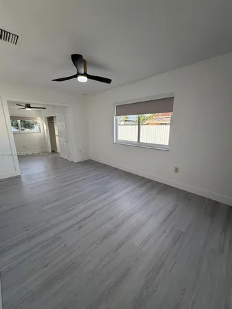 an empty room with wooden floor ceiling fan and windows