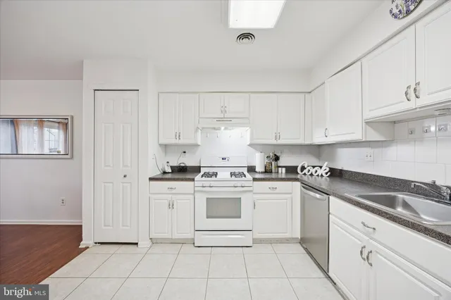 a white kitchen with stainless steel appliances granite countertop a stove a sink and white cabinets