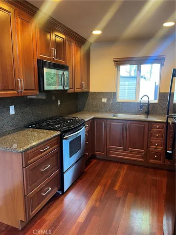 a kitchen with granite countertop wooden floors wooden cabinets a sink and a stove