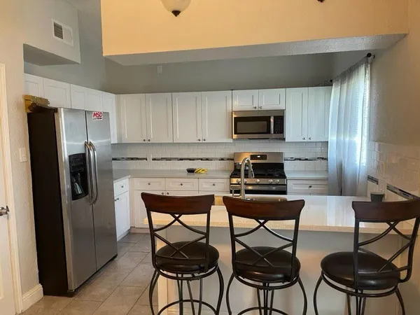 a kitchen with stainless steel appliances a refrigerator stove a sink and chairs