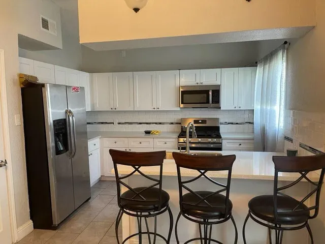 a kitchen with stainless steel appliances a refrigerator stove a sink and chairs
