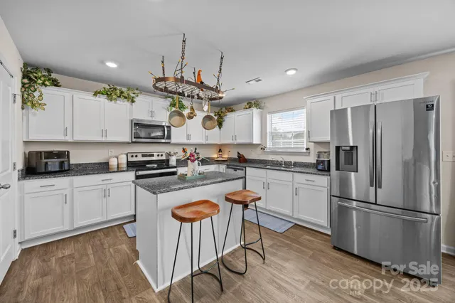 a kitchen with stainless steel appliances granite countertop a refrigerator a sink dishwasher a stove and white cabinets with wooden floor