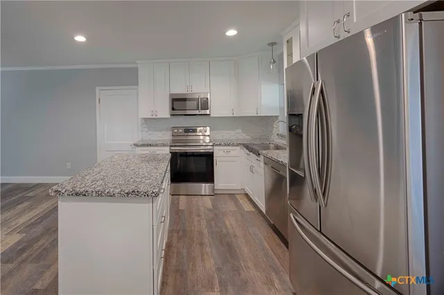 a kitchen with stainless steel appliances granite countertop a refrigerator a stove and a sink with wooden floor