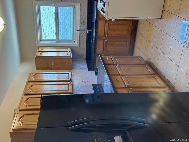 239-13 86th Avenue Queens, NY 11426 - Photo 4 of 12 Kitchen with refrigerator, light tile patterned flooring, black range, brown cabinets, and tasteful backsplash