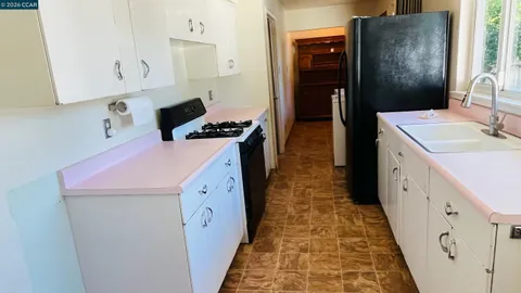 a kitchen with granite countertop a stove a sink a refrigerator and white cabinets