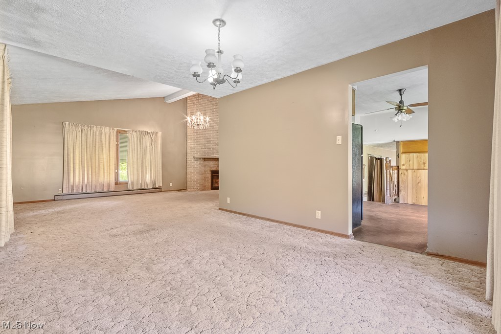 1165 Homeworth Road Alliance, OH 44601 - Photo 13 of 36 Unfurnished living room featuring a fireplace, carpet floors, vaulted ceiling, a textured ceiling, and ceiling fan with notable chandelier