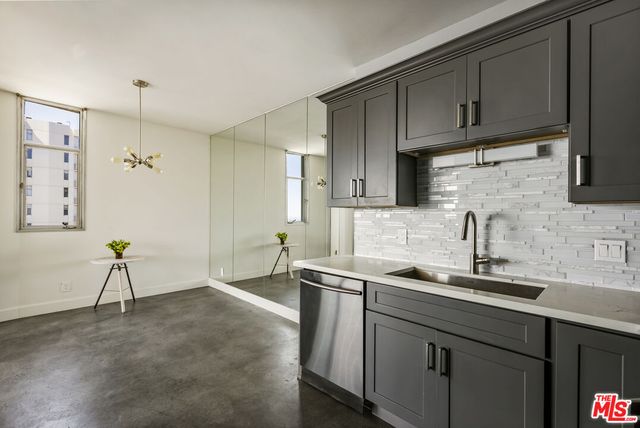 an empty room with wooden floor and way to kitchen