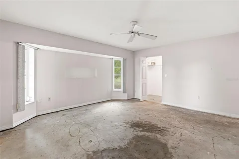 an empty room with chandelier fan and windows
