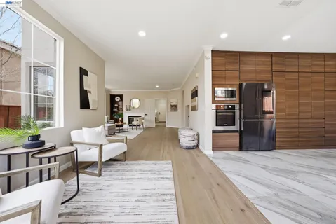 a living room with stainless steel appliances furniture wooden floor and a large window