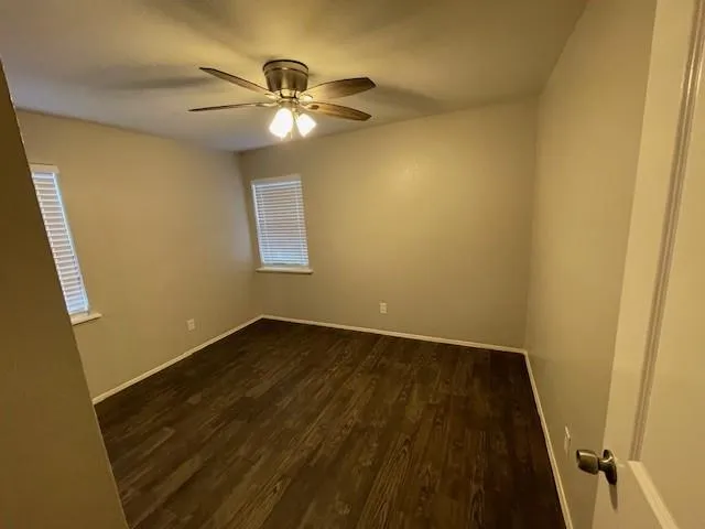 a view of an empty room with wooden floor and a ceiling fan