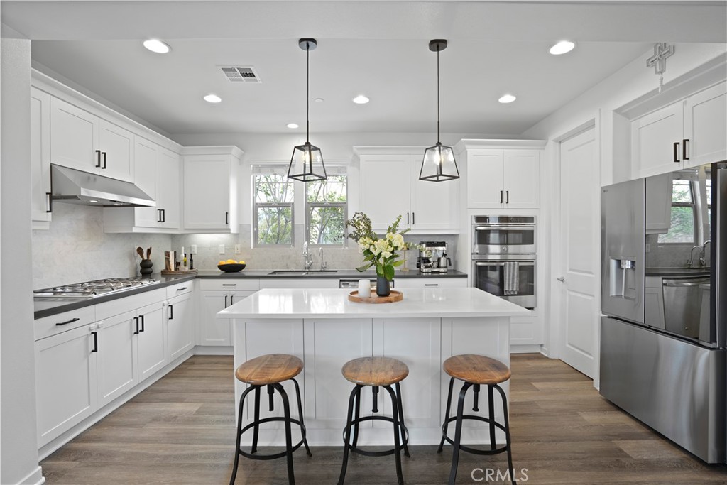 58 Vasto Street Rancho Mission Viejo, CA 92694 - Photo 16 of 66 a kitchen with stainless steel appliances granite countertop a stove top oven a refrigerator a sink and white cabinets with wooden floor