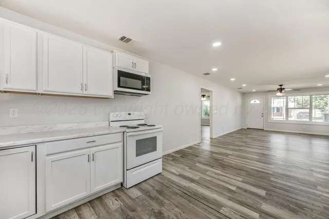 a kitchen with granite countertop a stove a sink and dishwasher with white cabinets