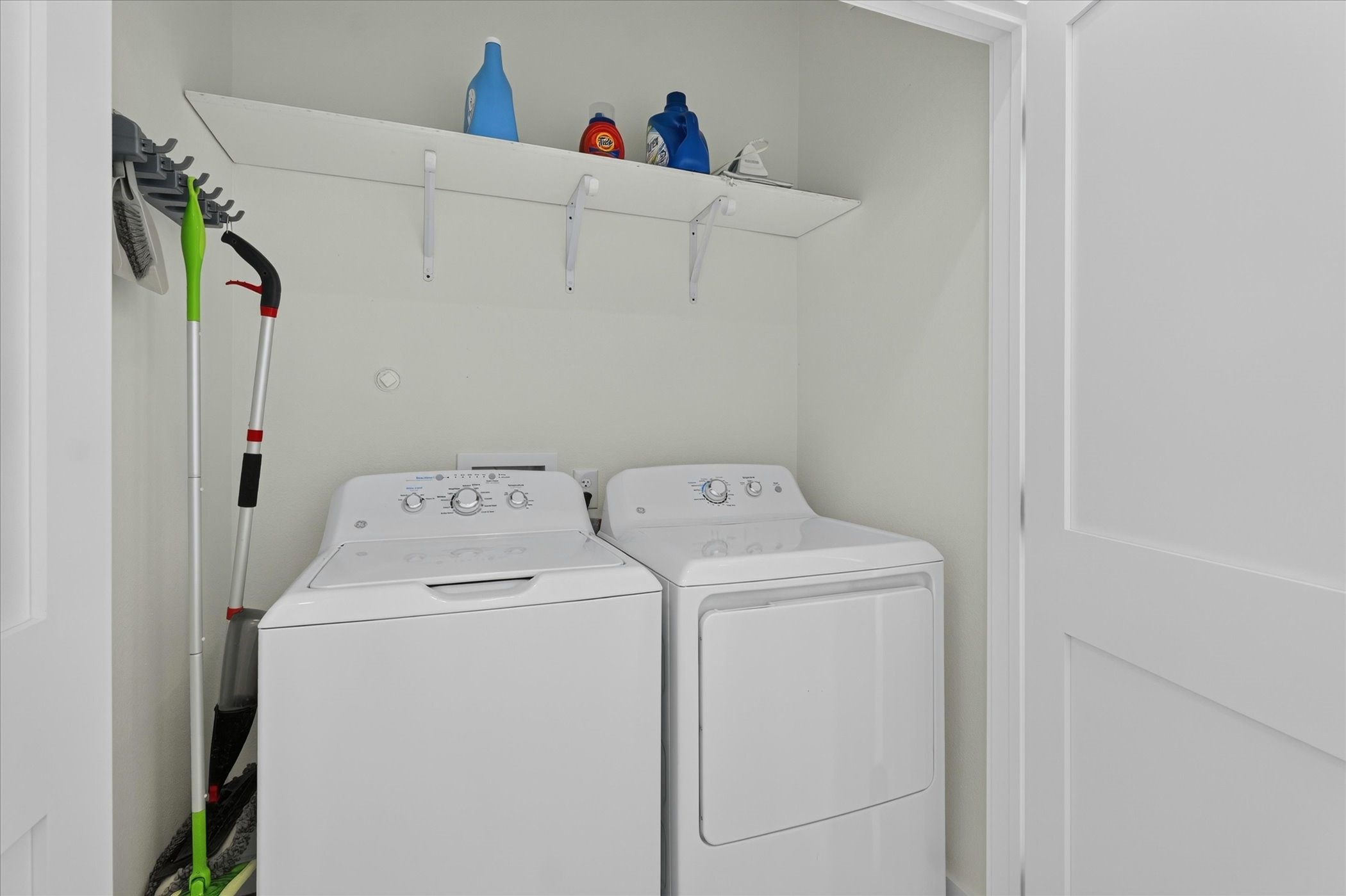 2000 Riverside Farms Road, Unit 8101 Austin, TX 78741 - Photo 35 of 41 This photo features a compact laundry area equipped with a washer and dryer, a shelf above for storage, and space for cleaning tools.
