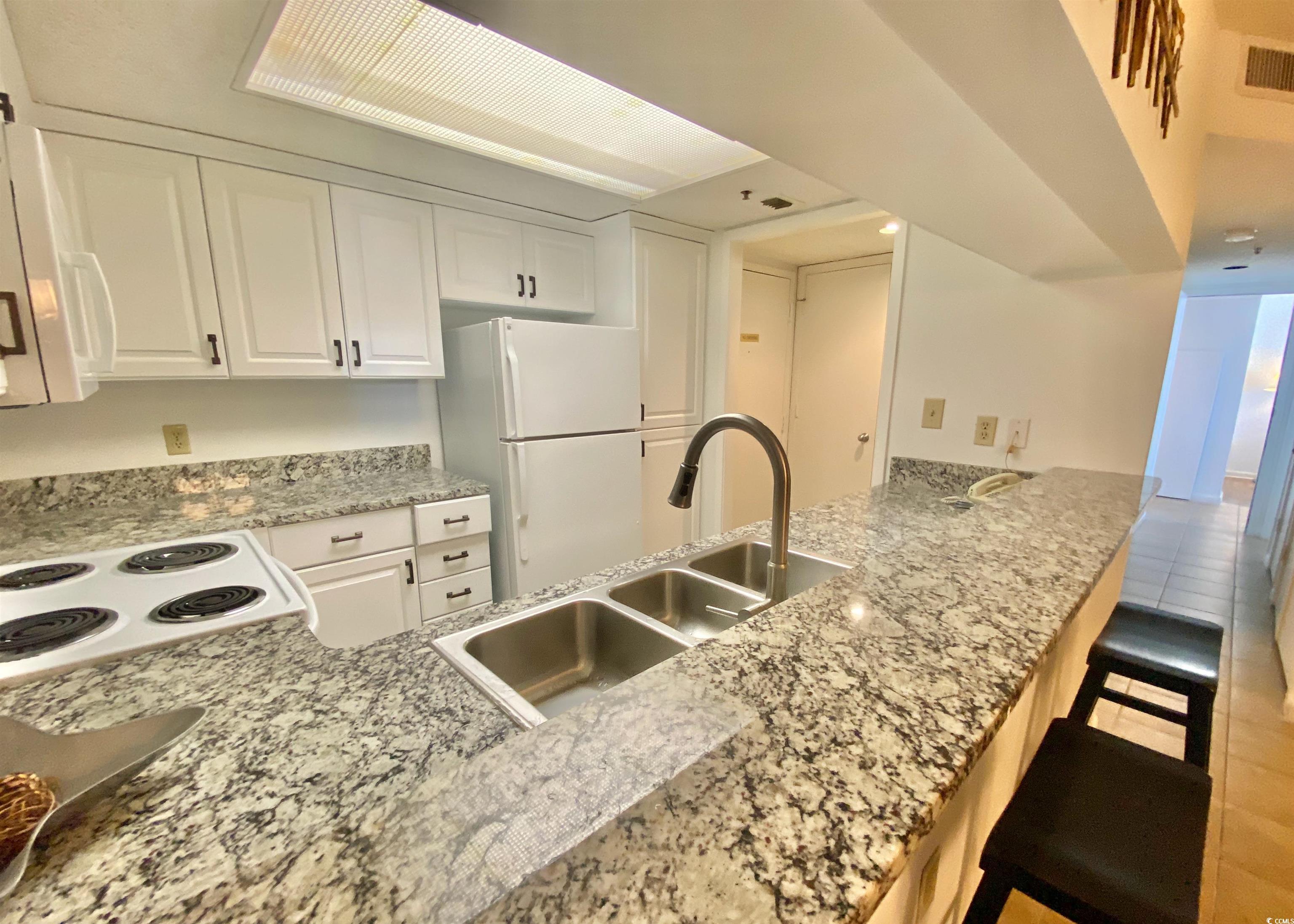 9820 Queensway Boulevard, Unit 206 Myrtle Beach, SC 29572 - Photo 11 of 40 Kitchen featuring a breakfast bar, kitchen peninsula, sink, white appliances, and white cabinetry