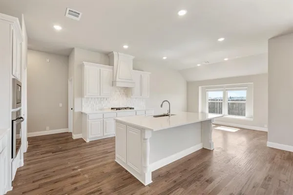 a large kitchen with stainless steel appliances granite countertop a white stove top oven and white cabinets with wooden floor