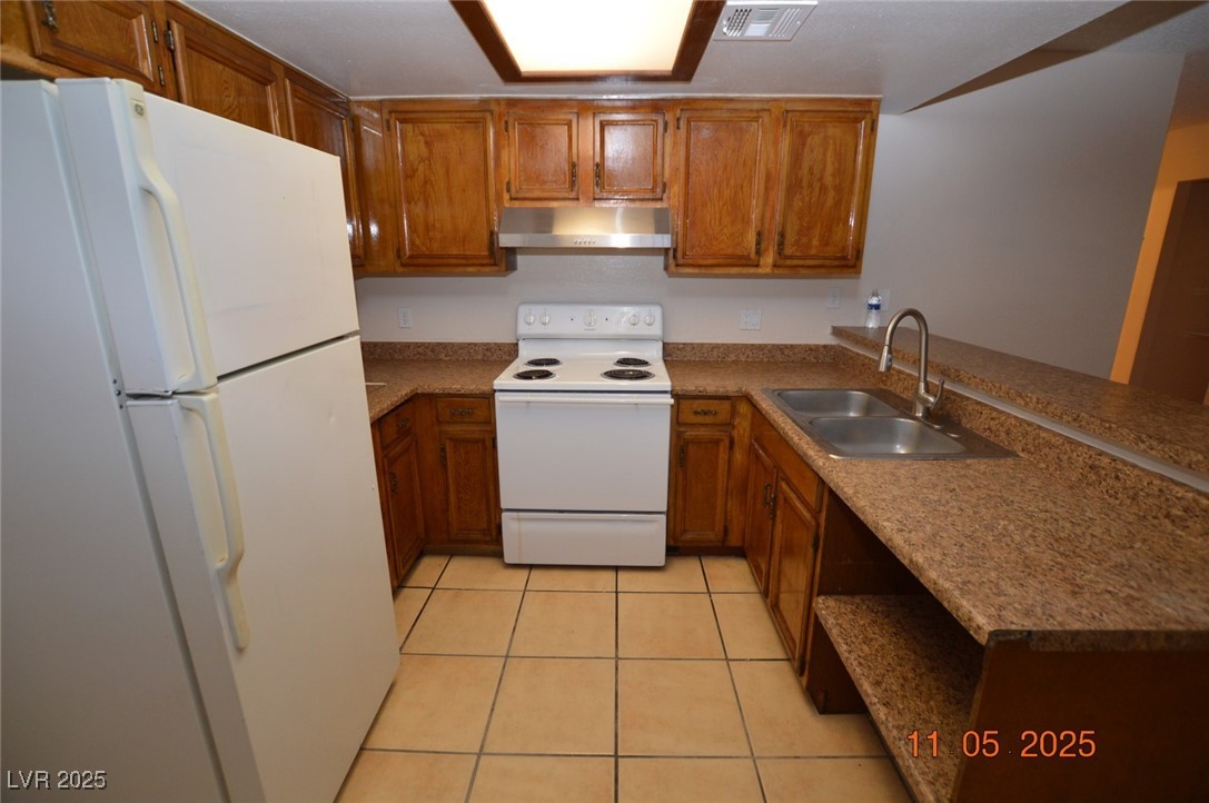 3240 North Mary Dee Avenue, Unit D North Las Vegas, NV 89030 - Photo 5 of 10 Kitchen with white appliances, brown cabinets, light tile patterned floors, extractor fan, and a peninsula
