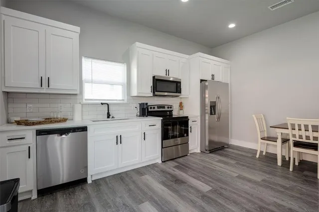 a kitchen with granite countertop a refrigerator stove microwave and white cabinets
